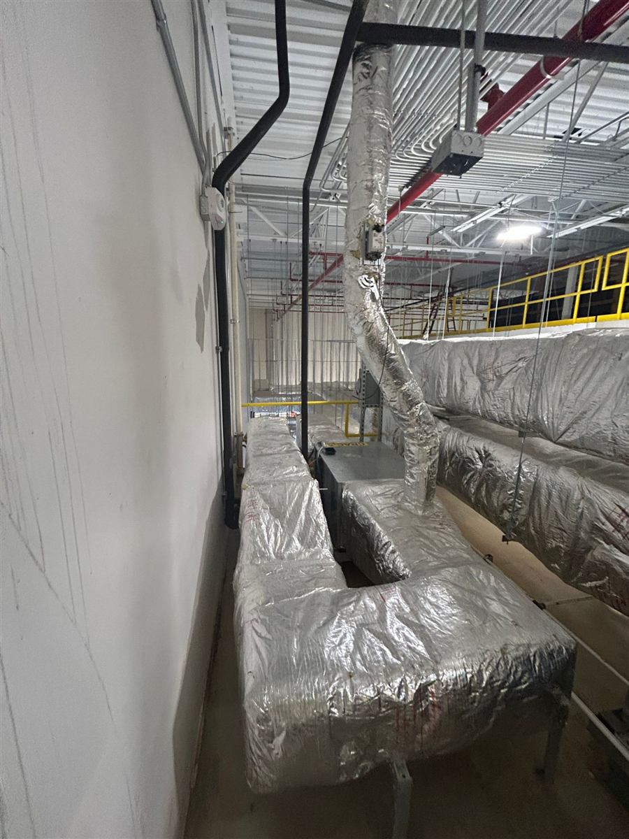 Insulated supply ductwork running along a wall above a mezzanine